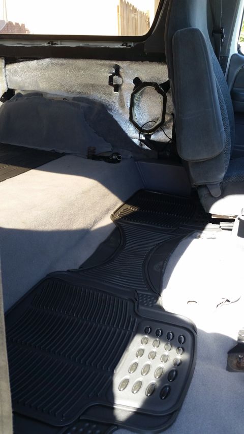 1992 Ford Bronco - The interior of a vehicle shows gray seats and black rubber floor mats, with insulation visible on the rear panel.