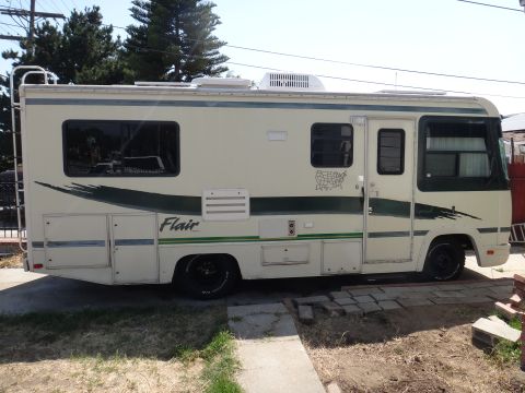 1995 Chevrolet P30 1 Ton - Step Van - The side view of a cream-colored RV with green accents is parked on a paved surface with some grass and dirt around it. The RV has tinted w…