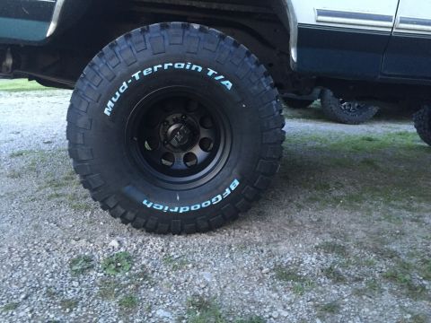 1994 Ford Bronco - Close-up of a BFGoodrich Mud-Terrain T/A tire and black wheel, with another vehicle in the background.