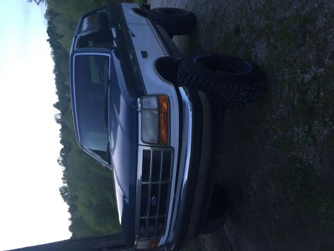 1994 Ford Bronco - A dark blue Ford Bronco is shown from a three-quarter front angle, parked on uneven ground.