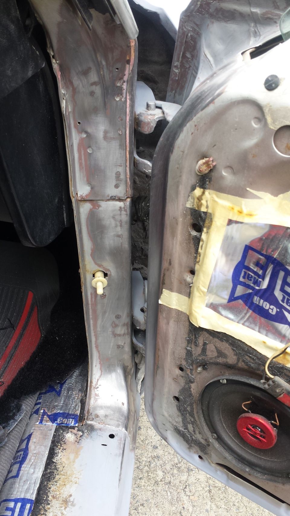 Close-up of a car's door jamb area, showing exposed metal and a speaker mounted inside the door panel