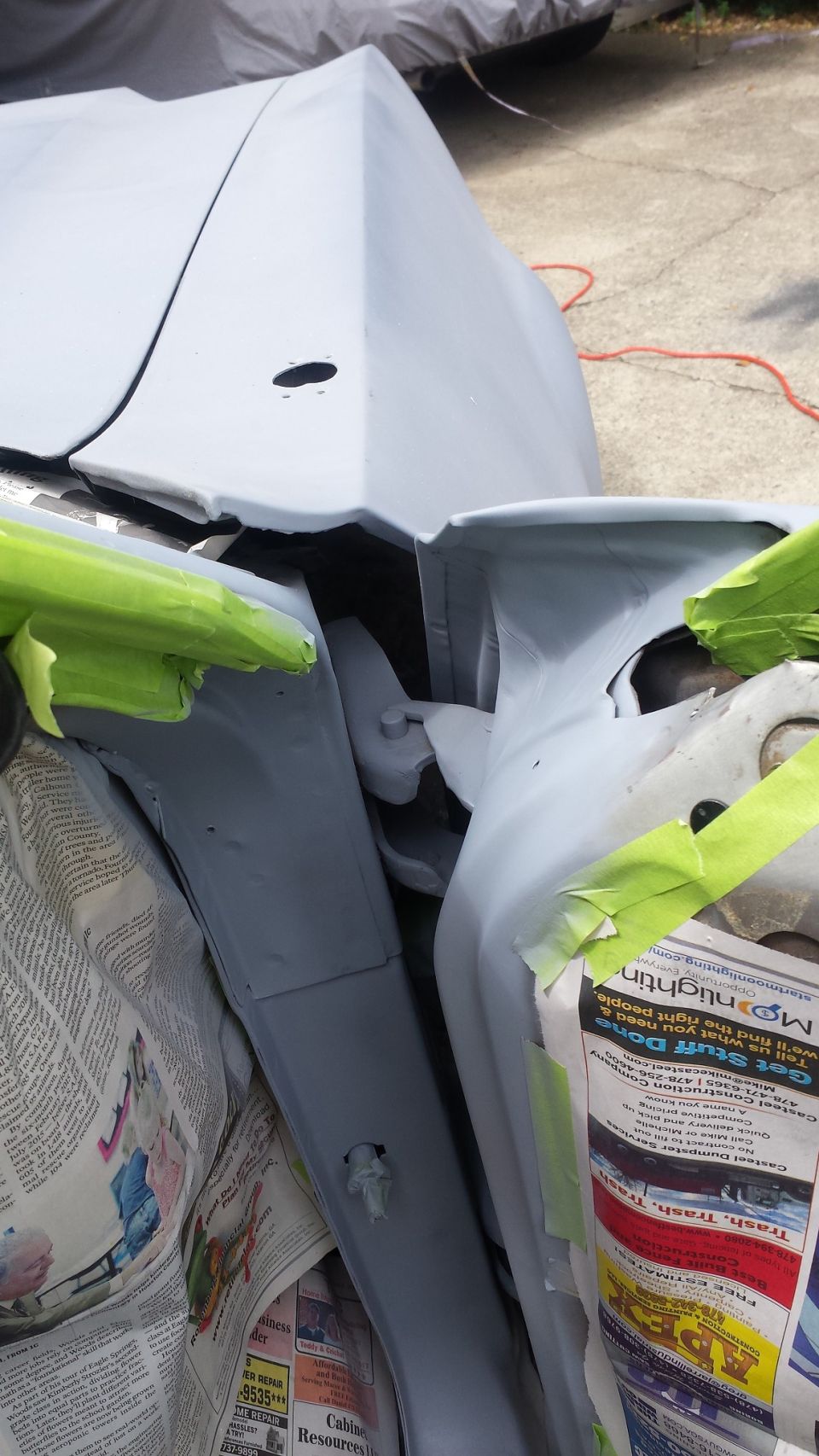 Car body panels prepped for paint, with green masking tape and newspaper covering parts
