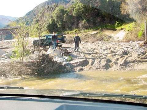 1988 Ford Bronco - Two men and a green SUV are stopped on a rocky riverbed, possibly after off-roading.