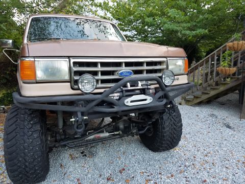 1988 Ford Bronco - This tan Ford truck features a custom bumper with a winch and auxiliary lights, suggesting off-road modifications.
