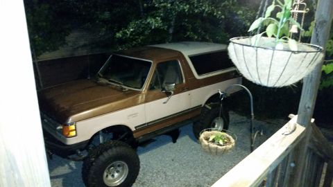 1988 Ford Bronco - This lifted Ford Bronco is parked in a driveway at night, with hanging plants nearby.
