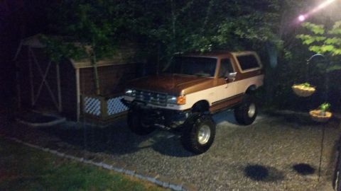1988 Ford Bronco - This lifted Ford Bronco is parked in a gravel driveway next to a wooden shed.