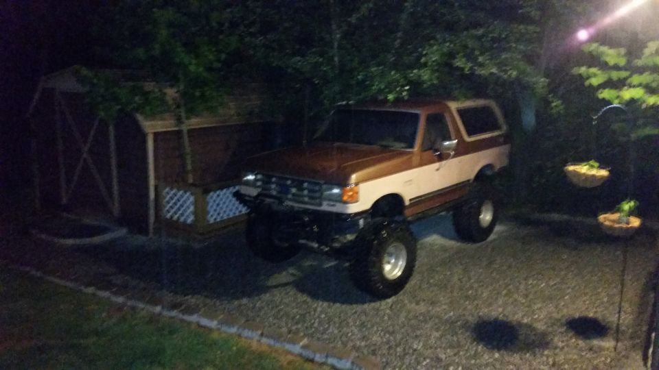 Brown and white lifted Ford Bronco parked next to a shed at night