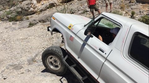 1979 Ford Bronco - A white Ford Bronco navigates a rocky, off-road path with two people standing in the background.