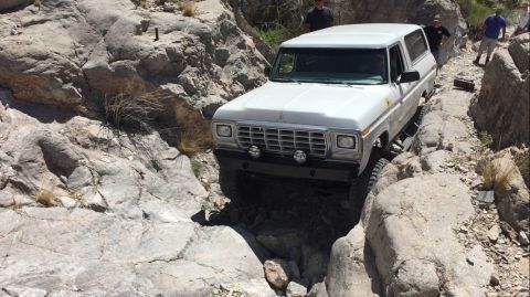 1979 Ford Bronco - White SUV carefully maneuvers through a narrow, rocky canyon with people observing.
