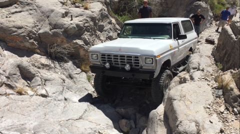 1979 Ford Bronco - A white 1979 Ford Bronco carefully maneuvers through a challenging rocky terrain on an off-road trail.