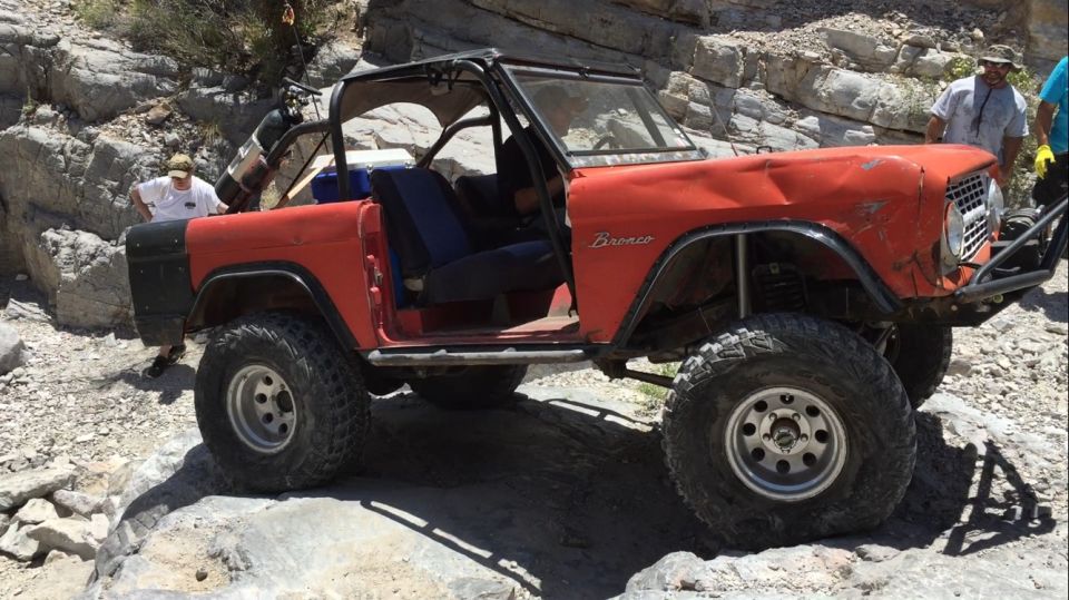 Red Ford Bronco with off-road tires on rocky terrain. A person is standing behind it