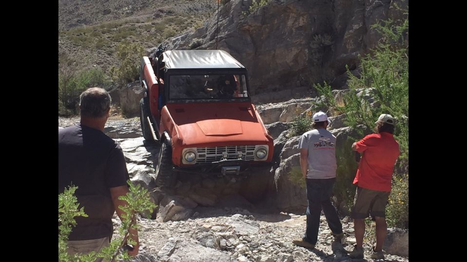 Orange off-road vehicle with a white soft top navigating a rocky trail, front view