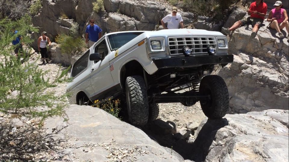 White Ford Bronco climbing over rocks on a trail. People watch from the side