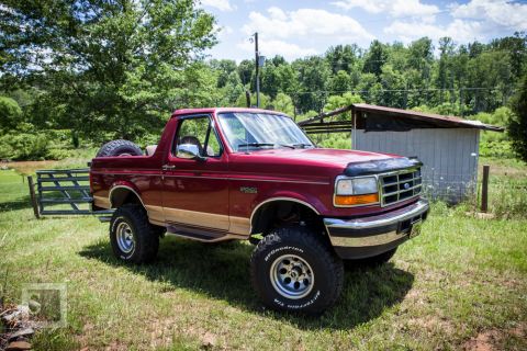 1995 Ford Bronco - This red 1995 Ford Bronco features tan lower body trim and a spare tire mounted on the rear tailgate.