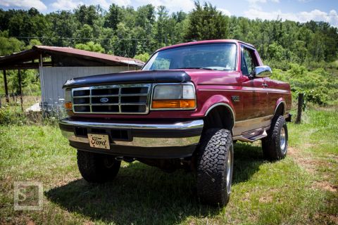 1995 Ford Bronco - This maroon Ford F-Series truck features a lifted suspension and large off-road tires.