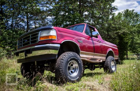 1995 Ford Bronco - This lifted 1995 Ford Bronco features a prominent grille and tan side trim, captured in a three-quarter front view.