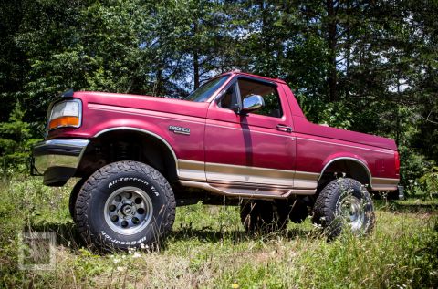 1995 Ford Bronco - This red 1995 Ford Bronco is parked in a grassy area surrounded by trees.