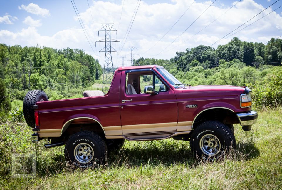 Red Ford Bronco parked in a grassy field with power lines overhead