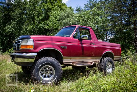1995 Ford Bronco - This red 1995 Ford Bronco features a two-tone paint scheme and a removable top, captured in a natural outdoor setting.