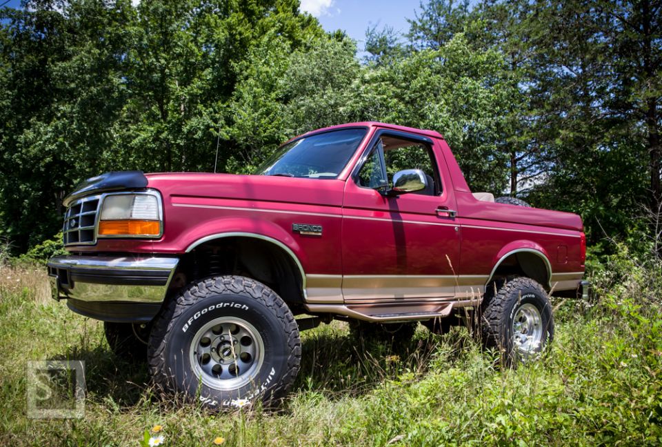Red 1995 Ford Bronco with removable top parked in grassy area