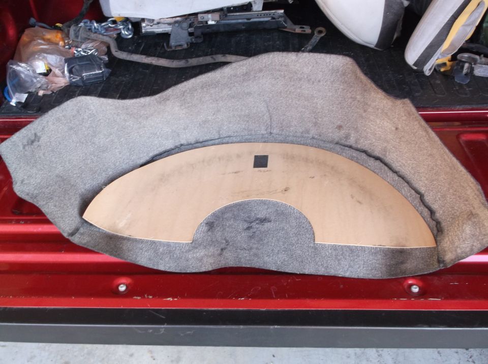 Car trunk liner with a cardboard template on top, showing a red truck bed