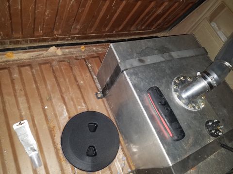 1988 Ford Bronco - A large metal fuel tank is installed in the cargo area of a vehicle, next to a tube of sealant and a round access plate.