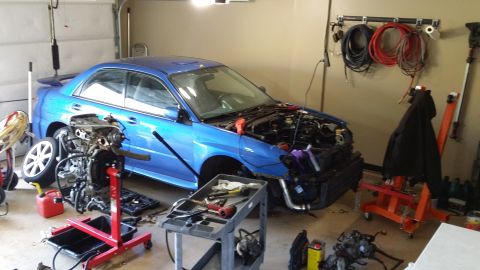 2007 Subaru Impreza - A blue Subaru Impreza is in a garage with its hood open and engine disassembled, surrounded by tools and parts.