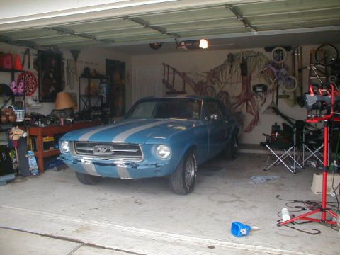 1967 Ford Mustang - A blue 1967 Ford Mustang with silver racing stripes is parked inside a garage.