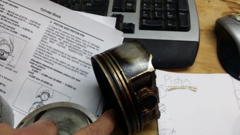 2007 Subaru Impreza - A damaged piston sits on a table next to a page from an engine repair manual detailing piston inspection.