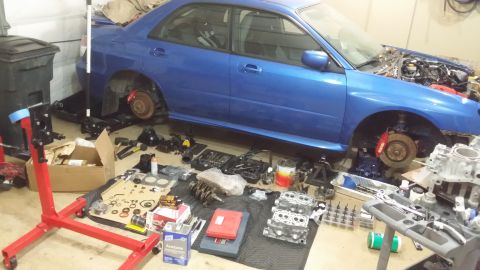 2007 Subaru Impreza - A blue 2007 Subaru Impreza is parked with its hood open and engine components laid out on the garage floor for a rebuild.