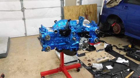 2007 Subaru Impreza - Blue Subaru EJ25 engine on stand, with parts laid out for rebuild. A blue Subaru WRX is in the background.