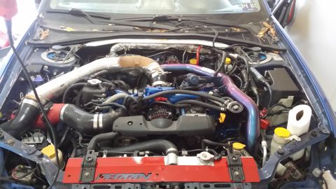 2007 Subaru Impreza - The engine bay of a blue Subaru shows extensive modifications, including a large intercooler and custom piping.