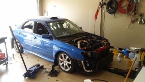 2007 Subaru Impreza - A blue Subaru Impreza sedan is in a garage with its hood open and front bumper removed, showing the engine.