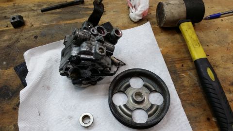 2007 Subaru Impreza - A disassembled power steering pump and pulley sit on a workbench next to a rubber mallet and other tools.