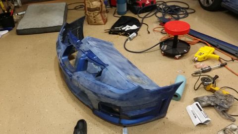 2007 Subaru Impreza - A blue car bumper, partially covered in body filler, sits on a garage floor surrounded by tools and supplies.