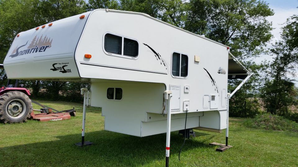 Snowriver truck camper with Super Slide, parked on grass with a tractor and mower behind it