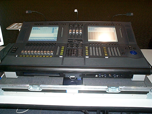 Black stage lighting control console with dual screens and faders on a road case