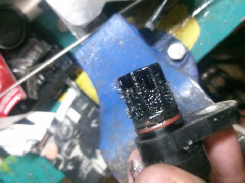 1996 Ford Bronco - A speed sensor is shown covered in metal debris, clamped in a blue vise.