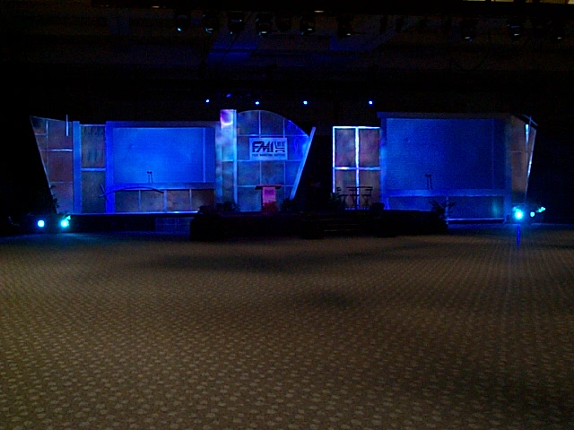 Blue-lit corporate stage set with two projection screens in an empty ballroom