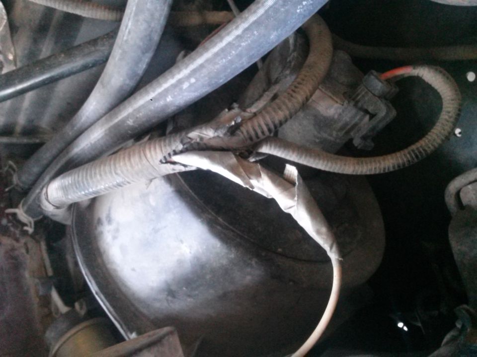 Close-up of frayed wiring harness and rubber hoses in a vehicle's engine bay