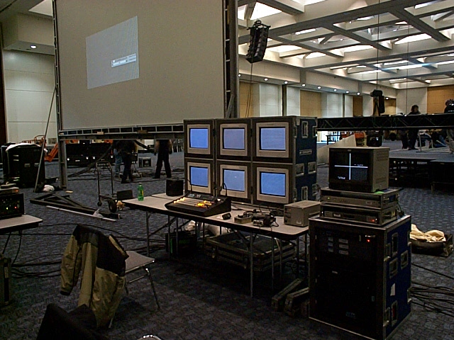 Setup with a large projection screen, multiple monitors, and audio/video equipment in a conference hall