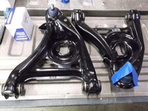 2001 Mercury Grand Marquis - Two black control arms are laid out on a surface next to a box of automotive parts.