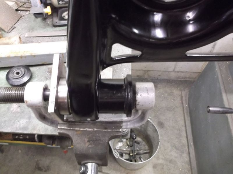 Black metal suspension component clamped in a vise with a threaded rod