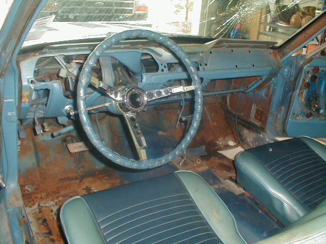 1967 Ford Mustang interior with blue dashboard, cracked windshield, and rusty floor pans