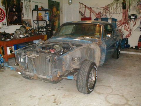 1967 Ford Mustang - This blue 1967 Ford Mustang coupe is in a garage, appearing to be undergoing restoration with its front end disassembled.