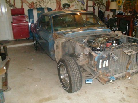 1967 Ford Mustang - A vintage Ford Mustang is partially disassembled in a garage, showing its engine and stripped front end.