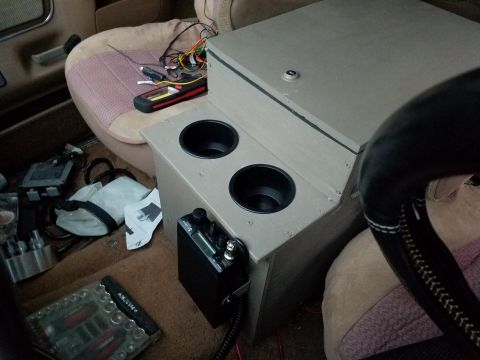1988 Ford Bronco - The interior of a vehicle features a custom-built console with cup holders and a CB radio, surrounded by various tools and bags.