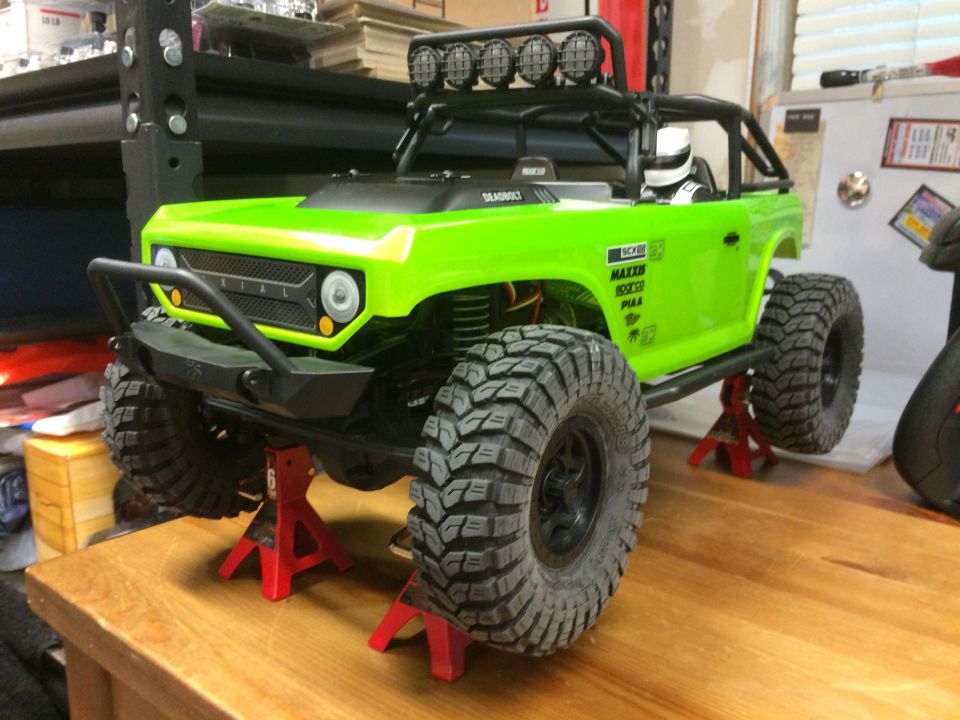 Green RC rock crawler truck with large tires, on red jack stands. "AXIAL" visible on grille