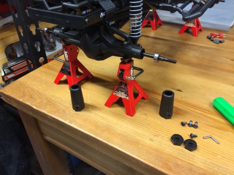 1989 Ford Bronco - RC car axle assembly is supported by red jack stands on a wooden table.