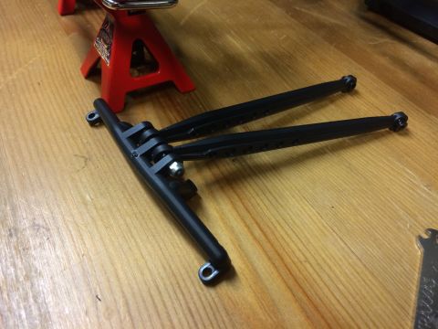 1989 Ford Bronco - Black plastic suspension arms are shown on a wooden surface, next to a red jack stand.